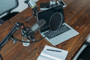 laptop and notebook on wooden table near microphone in broadcasting studio
