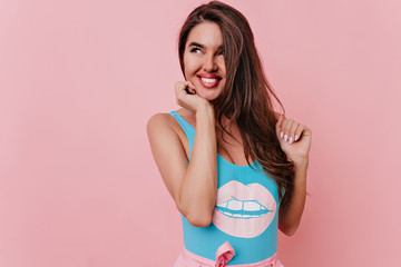 Fototapeta na wymiar Carefree girl with long hairstyle looking away with smile. Studio shot of dreamy brunette woman in blue attire isolated on pink background.