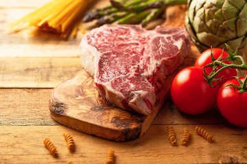 Fresh raw piece of marbled beef steak with fresh vegetables and Italian spaghetti, on a roasting board, on a wooden background. Restaurant menu, home menu. Delicious food, gastronomy