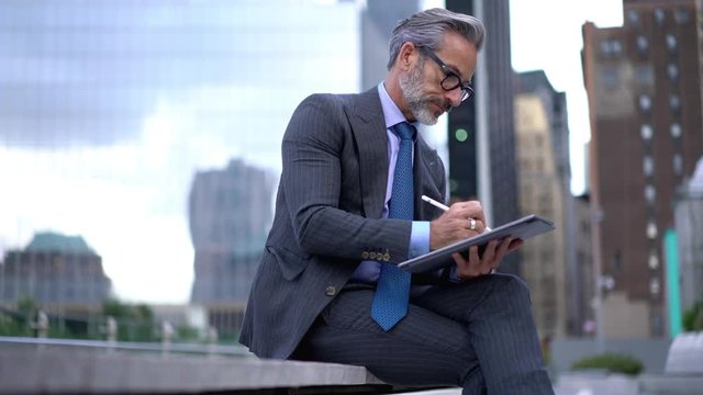  Mature male entrepreneur working with startup project via application on digital tablet, successful professional in optical spectacles making notes of information in spp on touch pad