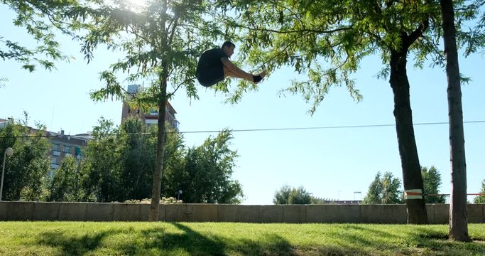 Young man performing as acrobat and training with slackline outdoors. Athlete doing sport activity and exercising with trickline in city park. Slow motion