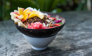 smoothie bowl in a coconut shell plate with with strawberries, chia seeds, banana, granola, flower on wooden background