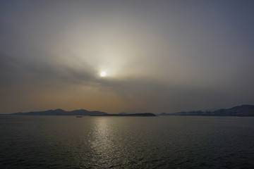 Fototapeta na wymiar Piraeus, Greece: Sunset over islands in the Saronic Gulf (Gulf of Aegina) reveals a large amount of dust pollution in the atmosphere.