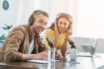 cheerful radio host looking at camera while sitting near pretty colleague