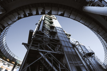 Wide angle shot from the ground of a contemporary building of an oil refinery or a modern fuel factory facility in an industrial zone, with a round bridge around, many pipes, and iron beams