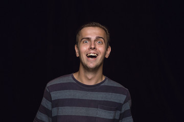 Close up portrait of young man isolated on black studio background. Photoshot of real emotions of male model. Crying throught laughting and smiling. Facial expression, human emotions concept.