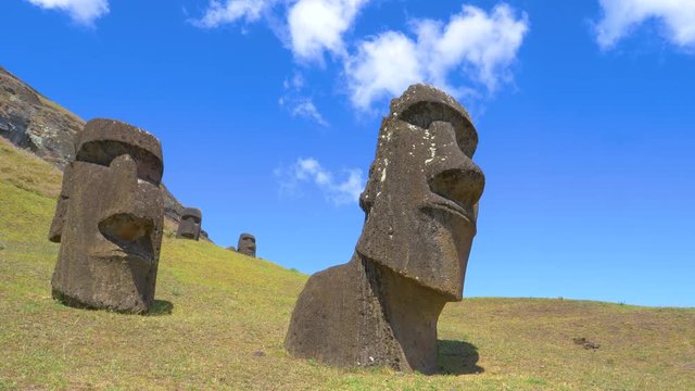 AERIAL, LOW ANGLE: Cinematic shot of exotic island landscape and fascinating moai statues. Ancient statues made of black stone are scattered around the grassfields under the volcano on Easter Island.