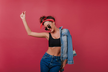 Enthusiastic sporty girl in sunglasses dancing on claret background. Studio shot of pleased...