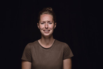 Close up portrait of young woman isolated on black studio background. Photoshot of real emotions of female model. Crying, sad, dreary and hopeless. Facial expression, human emotions concept.