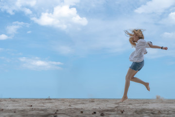 female making jump on sandy beach with blue sky
