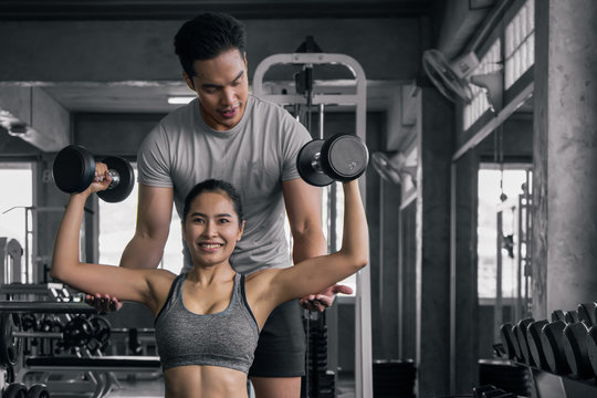 male trainer training female working out with dumbbells wieght lifting in gym