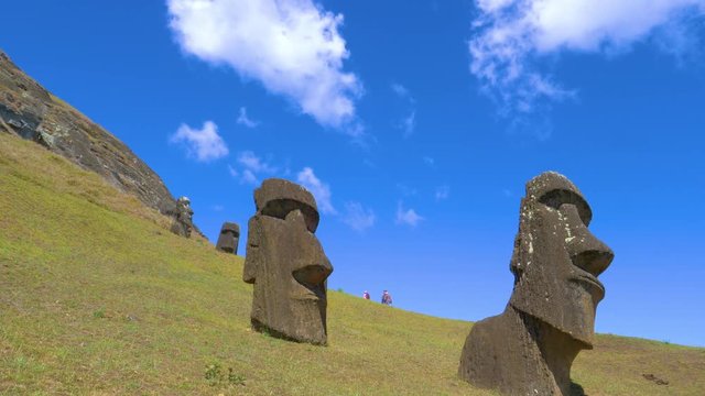 LOW ANGLE: A group of curious tourists hiking around the grassy hills and observing moais on Easter Island. Travelers exploring the famous volcanic statues scattered around remote exotic island.