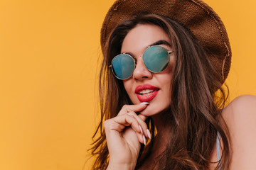Close-up portrait of pensive young woman in sparkle sunglasses. Studio shot of lovable dark-haired girl wears vintage brown hat.