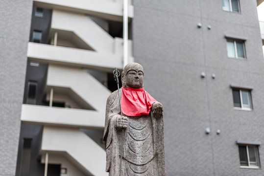 Osaka, Japan Jizo statue with red bib isolated with background of modern apartment building in downtown city