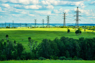 High voltage transmission towers on green grassland at sunny summer day  