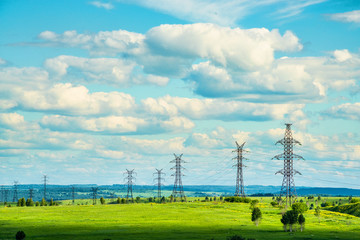 High voltage transmission towers on green grassland at sunny summer day  