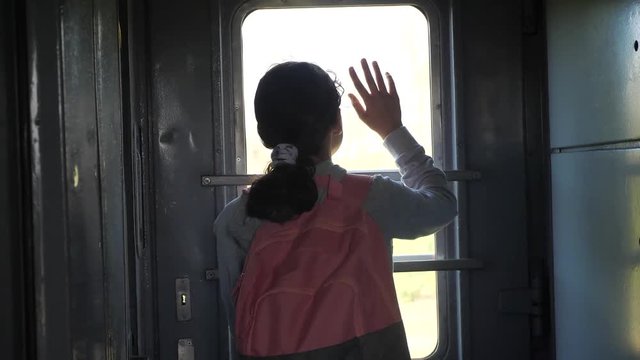 little teenage girl is a backpacker traveling by train lifestyle . travel transportation railroad concept. tourist school girl in the train wagon with backpack looking out the window waving his hand