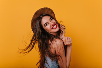 Refined young woman with tanned skin looking over shoulder with sincere laugh. Indoor portrait of graceful long-haired girl with dark hair.