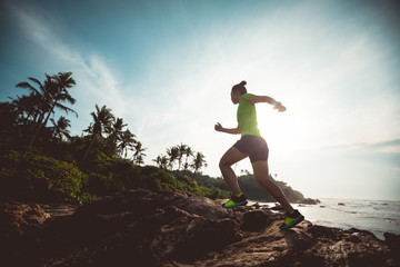 Young fitness woman trail runner running to rocky mountain top on seaside