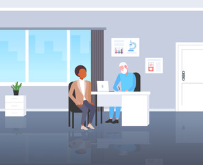 patient receiving a prescription african american man having consultation with senior doctor sitting at workplace medicine and healthcare concept modern hospital medical office full length flat