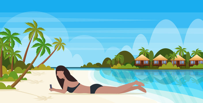 bikini woman sunbathing girl in swimsuit using smartphone social media communication summer vacation concept bunglow house landscape background full length horizontal