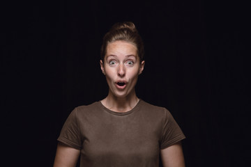 Close up portrait of young woman isolated on black studio background. Photoshot of real emotions of female model. Wondering, exciting and astonished. Facial expression, human emotions concept.