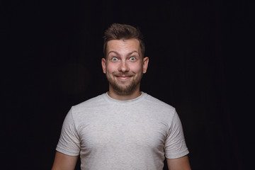 Obraz premium Close up portrait of young man isolated on black studio background. Photoshot of real emotions of male model. Wondering, exciting and astonished. Facial expression, human emotions concept.