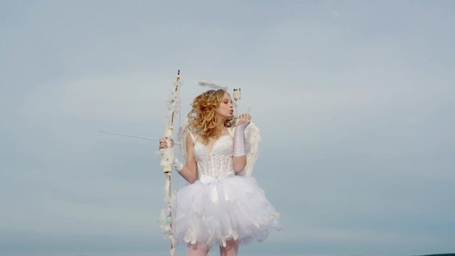 A beautiful teen with blonde curly hair and a bow and arrow as cupid - Valentines Day. Space for text. St Valentines day. Real fairy from magical stories