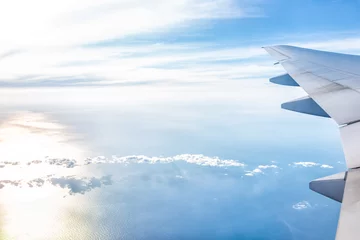Poster White airplane in blue sky with view from window high angle during sunny day with plane wing and sun setting above horizon with light path © Kristina Blokhin