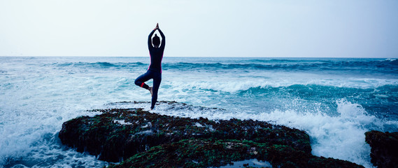 Young woman practice yoga at the seaside coral cliff edge