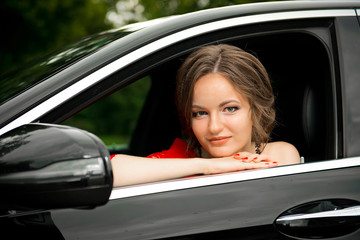 Fototapeta na wymiar Girl in a red dress driving a black car close-up.