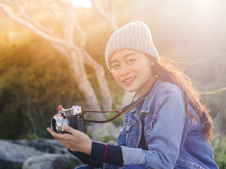 Happy Asian tourist holding vintage camera with nature background and rim light.