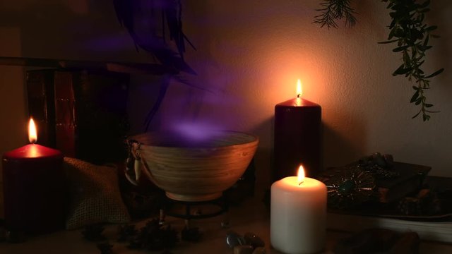 Detail of a potion making witch room, with purple steam coming out from a wooden bowl, animal teeth hanging from it, candles with flickering flames, old books, glasses and herbs, dust flying around