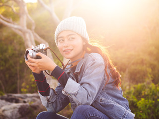 Happy Asian tourist holding vintage camera with nature background and rim light.