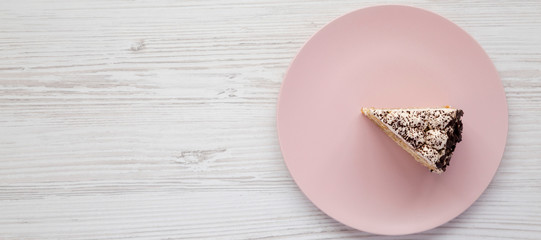 Fototapeta na wymiar A piece of tiramisu cake on a pink plate on a white wooden table, top view. Space for text.