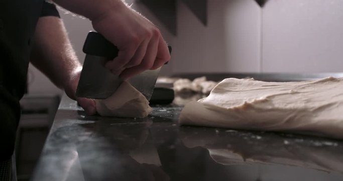 Stretching pizza dough in the back of a kitchen and cutting it into balls. Authentic Neapolitan Pizza cooked in a wood fire oven.
