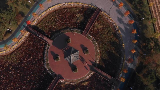 Aerial Zenithal gentle lowering above island in a park and people reaching an ancient asian pavilion