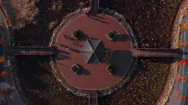 Aerial Zenithal gentle rise up above island in a park and people reaching an leaving from an asian pavilion