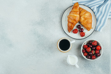 Food background. Coffee, croissants and berries for breakfast on light concrete background. Top view with copy space