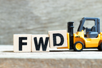 Toy forklift hold letter block D to complete word FWD (Abbreviation of forward) on wood background
