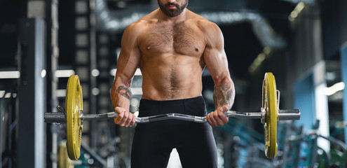 Fototapeta na wymiar Strong man with naked torso training hard with heavy barbell