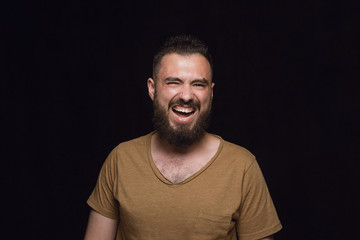 Close up portrait of young man isolated on black studio background. Photoshot of real emotions of male model. Smiling, feeling crazy happy, laughting. Facial expression, human emotions concept.