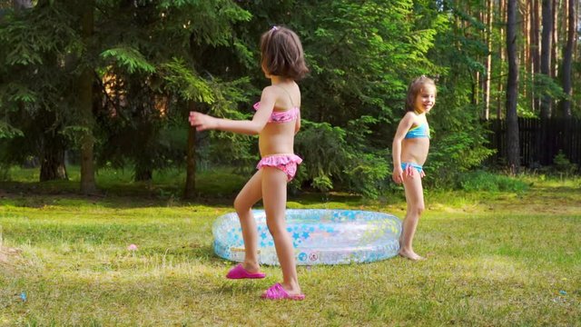 Two little girls playing with water balloons by pool on summer time