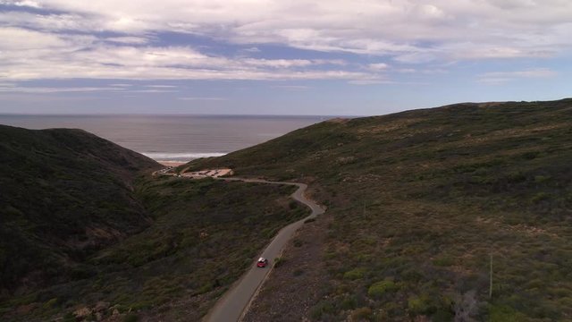 Praia do castalejo aerial red car driving single road to the beach with surfboards on the roof flysing over to beach. Flying drone shot