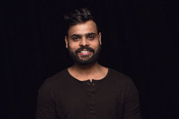 Close up portrait of young man isolated on black studio background. Photoshot of real emotions of male model. Smiling, feeling happy. Facial expression, pure and clear human emotions concept.