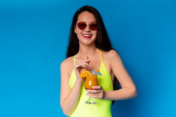 Positive woman enjoying tropical cocktail, wearing sunglasses and swimsuit