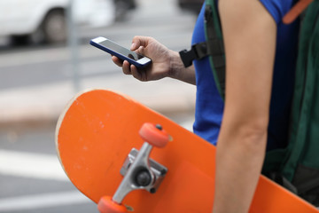 Woman with skateboard in hand using smartphone in modern city