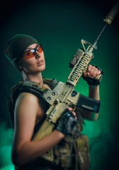 Obraz premium the girl in military special clothes posing with a gun in his hands on a dark background in the haze