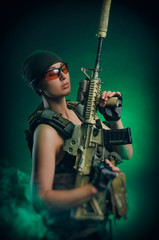 the girl in military special clothes posing with a gun in his hands on a dark background in the haze