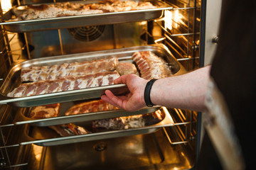 Smoked meat products in the oven smokehouse. A man holding a tray of smoked meat products